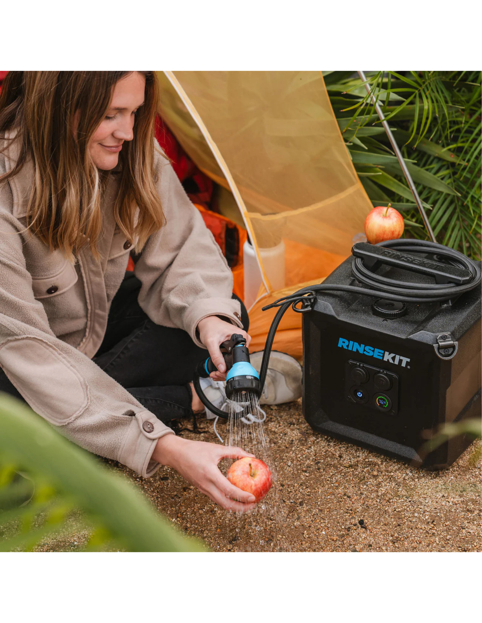 RinseKit Cube portable shower rinsing apple at campsite near tent