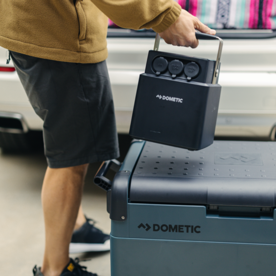 Person holding a Dometic portable power station over a Dometic cooler outdoors.