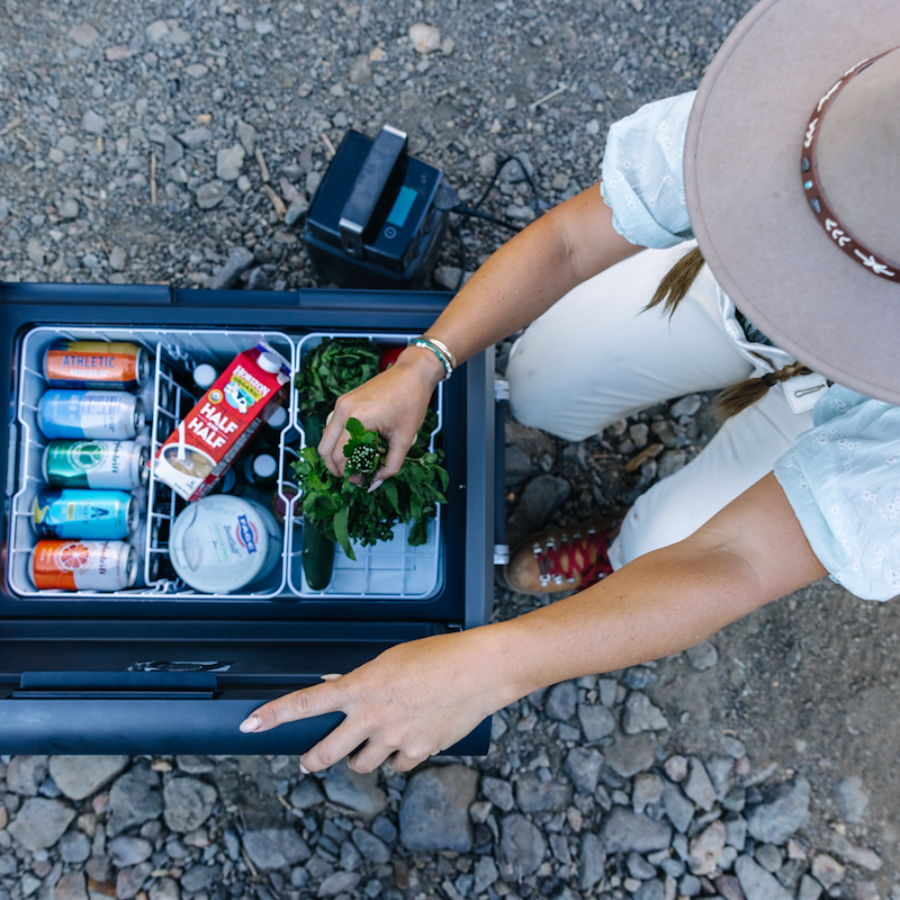 Person reaching into a cooler filled with snacks and drinks outdoors.